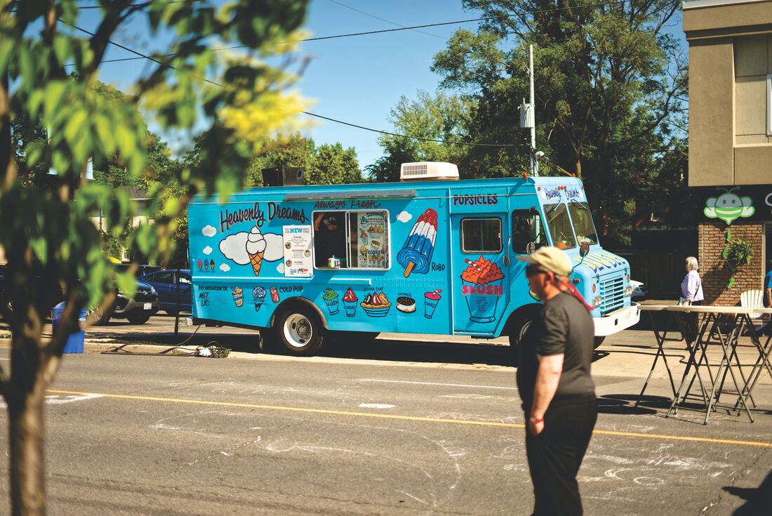 Neighborhood residents hear music from a blue ice cream truck featuring images of frozen treats.