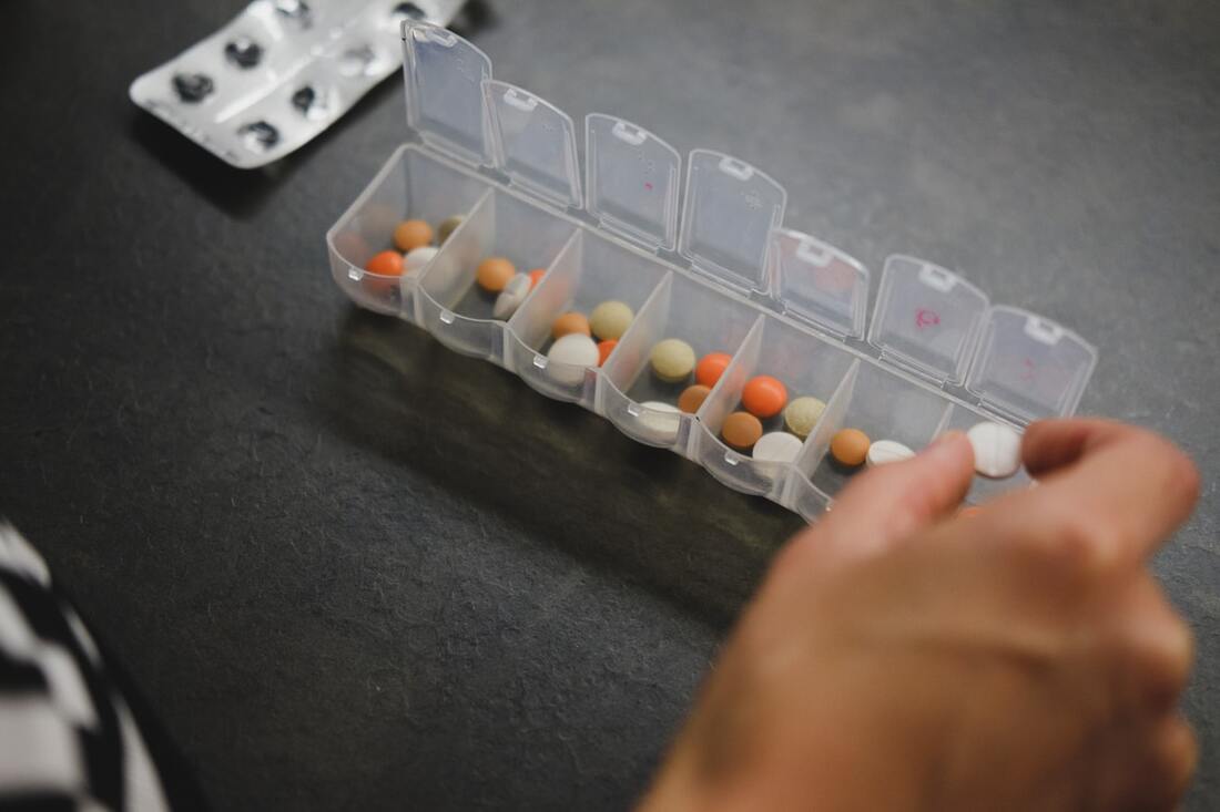A hand places a pill into a seven-day pill organizer box.