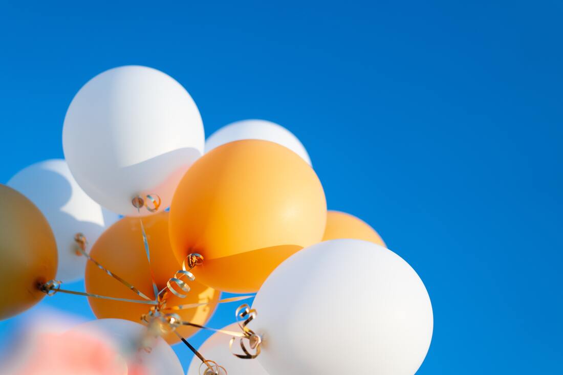 Orange and white balloons float against a blue sky, celebrating a Lancaster hearing aid company.