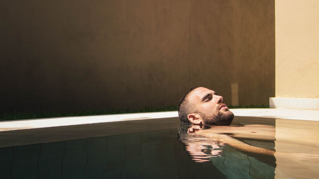 man with tinnitus and hearing loss rests head with eyes closed while relaxing in a pool