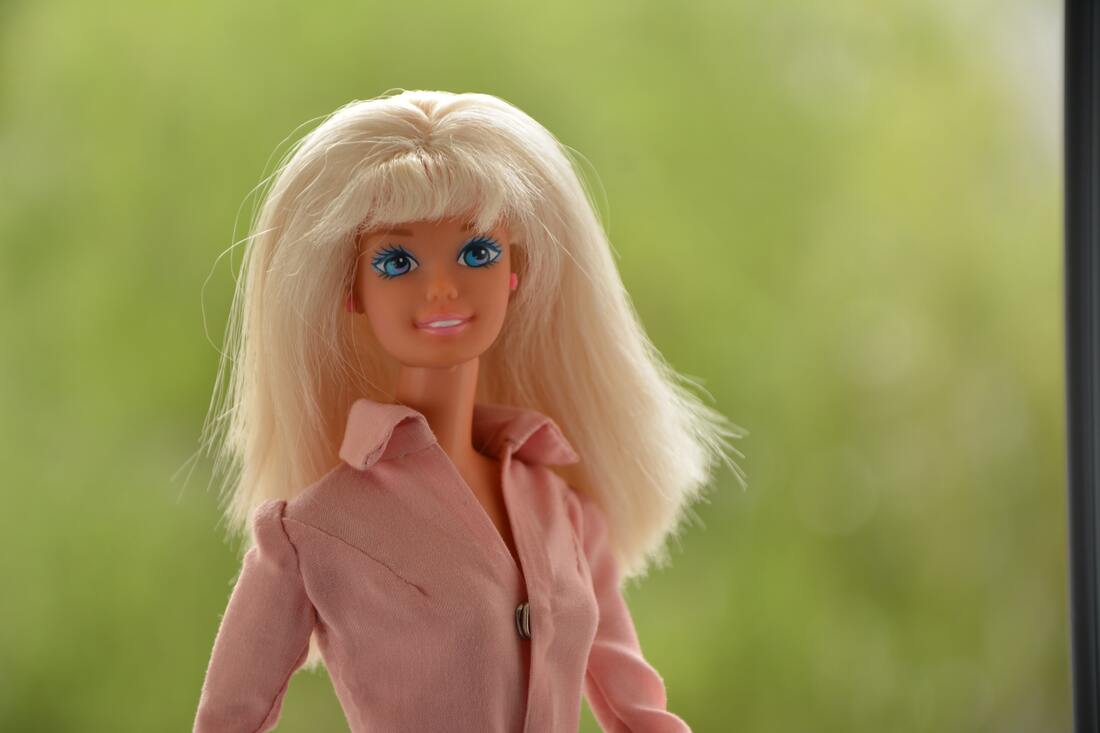 A blonde Barbie doll with a pink button down shirt wears hearing aids.
