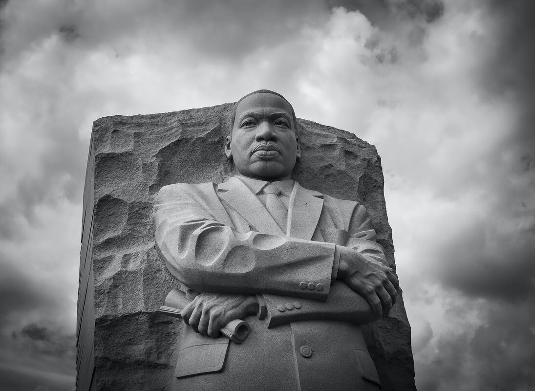 black and white photo of martin luther king jr statue with arms crossed holding rolled up dream speech