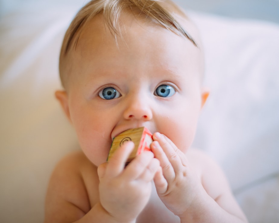 blonde haired blue eyed baby with wooden block in mouth has hearing loss