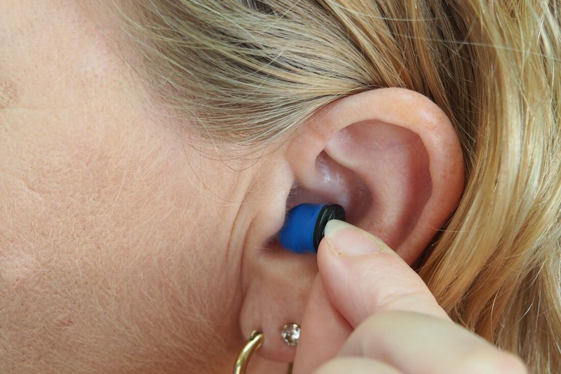 blonde haired woman removes blue and black hearing aid from ear