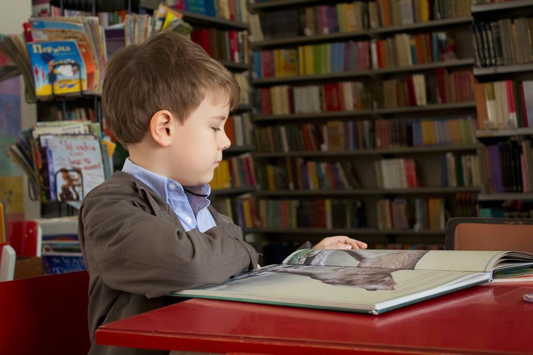 boy with hearing aids sits in library and reads book