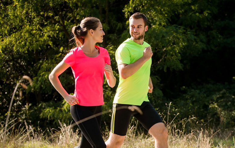 brunette_haired_woman_with_hot_pink_t-shirt_black_workout_leggings_wears_hearing_aids_while_jogging_and_talking_on_outdoor_trail_in_lancaster_to_man_with_neon_green_shirt_and_black_workout_shorts
