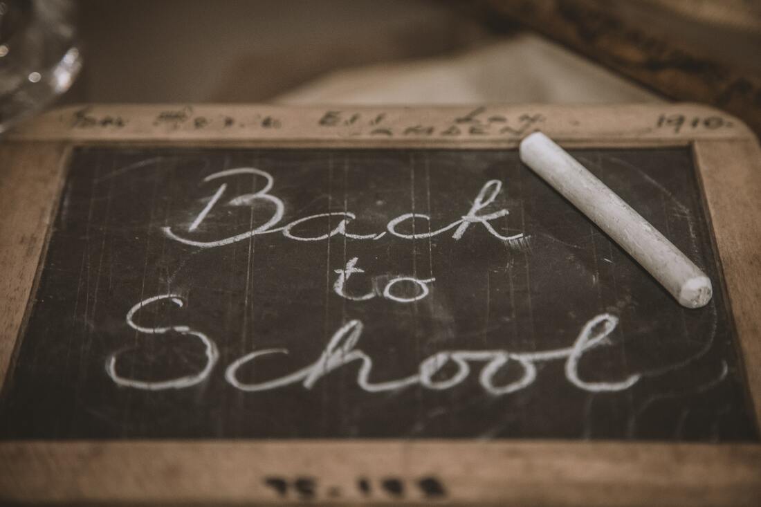A small chalkboard with “Back to school” written in white chalk with a piece of chalk on the board.