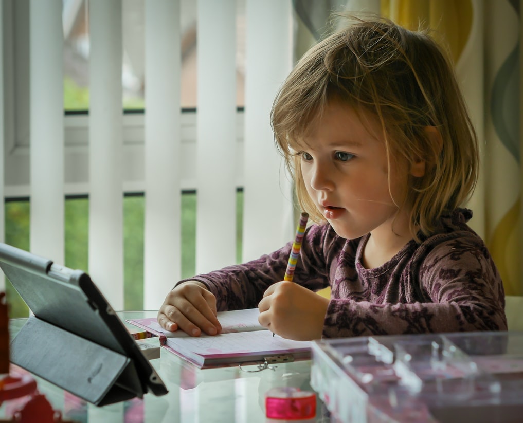 child with hearing loss looks at tablet and writes in notebook