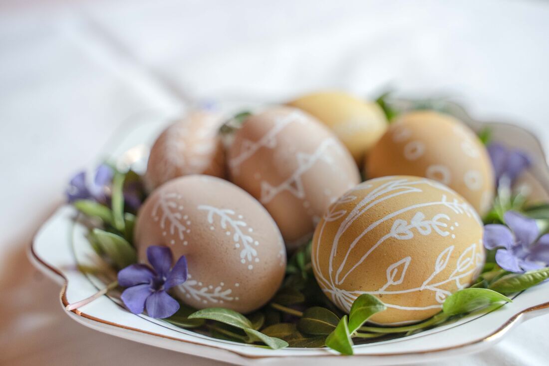 A plate features decorated Easter eggs on a bed of violet flowers with green leaves.