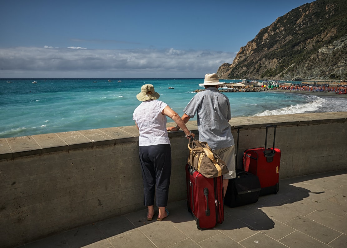 man and woman manage tinnitus while traveling to beach and looking at the ocean with luggage