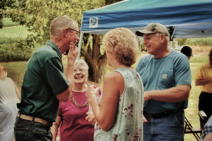 Old adults with hearing aids talk to each other and laugh outdoors in Lancaster County.