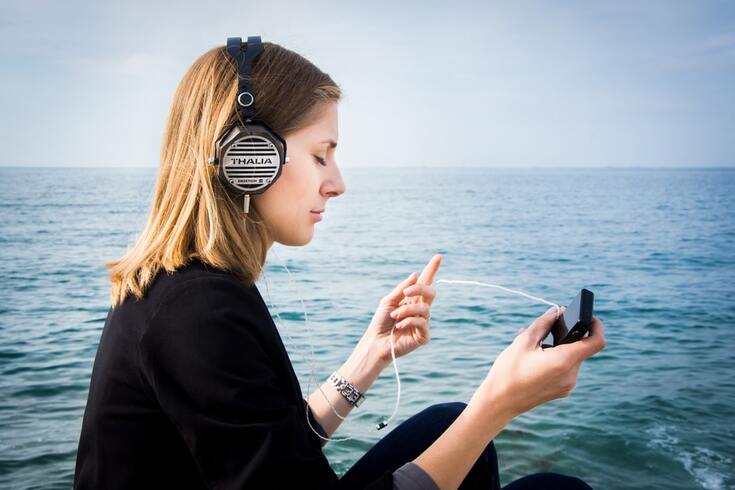 woman listens to music through headphones by the water