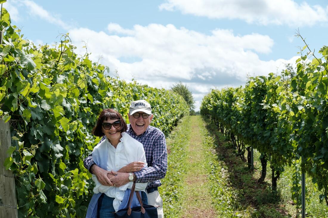 elderly couple with hearing aids embrace and laugh in vineyard