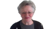 elderly_woman_with_grey_white_hair_glasses_black_sweater_grey_shirt_smiles_from_hearing_clearly_with_new_hearing_aids