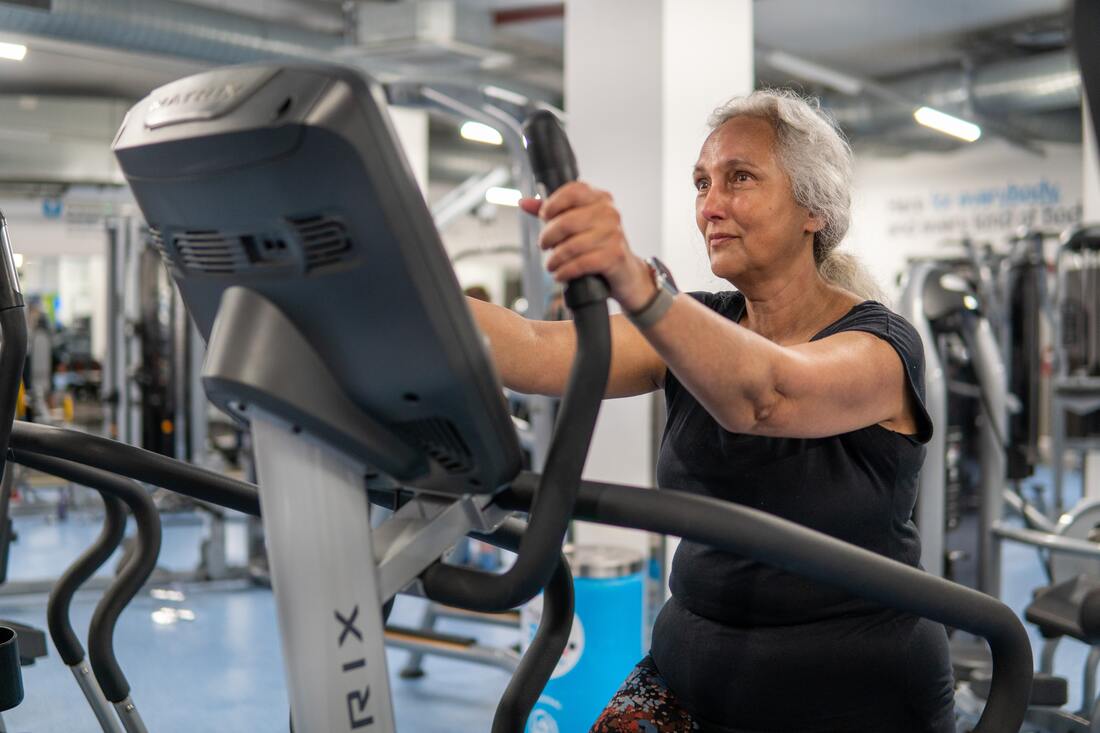 An old woman exercises on gym equipment in a public gym to improve her hearing and overall health.