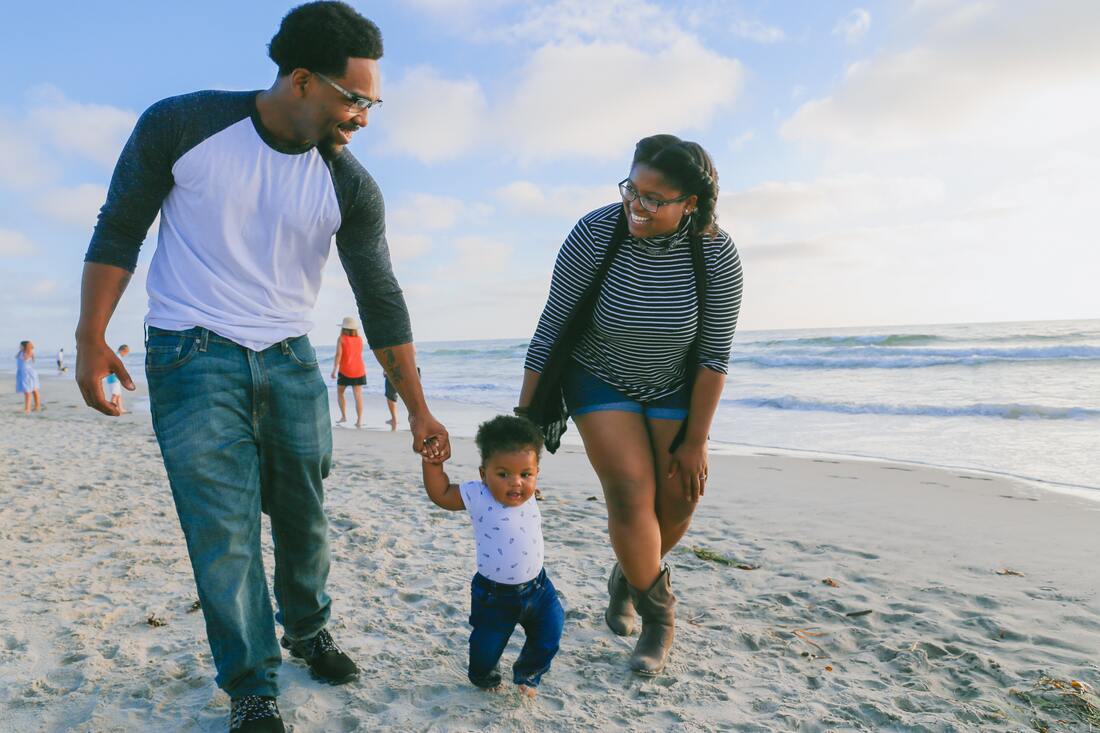 father_with_glasses_holds_child's_hand_while_walking_on_beach_with_mom_listen_to_laughter_and_sounds_of_ocean_waves_crashing_mt_gretna_lake_and_beach