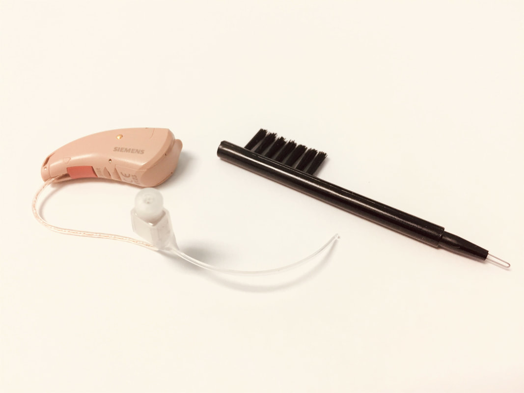 flesh toned hearing aid and black cleaning brush cleaning tool