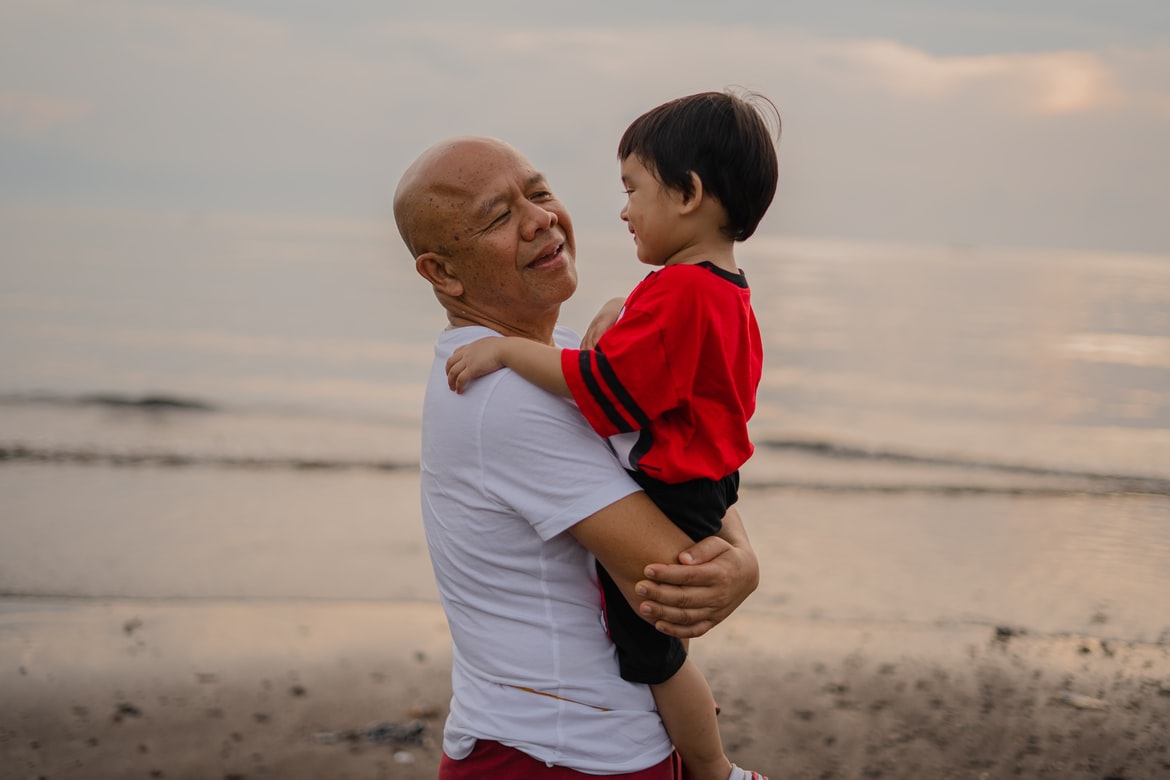 grandfather in white t-shirt has hearing loss wears in the ear hearing aids while holding grandchild in red and black shirt