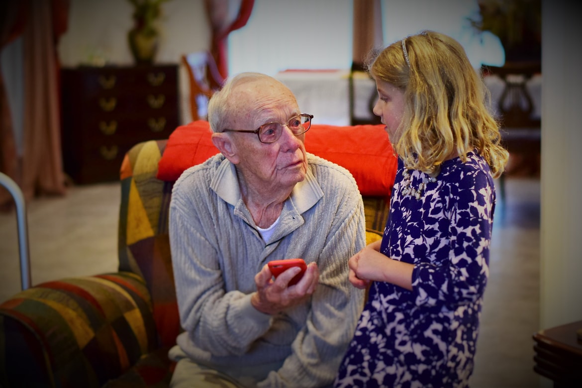 grandfather shows grandchild how to use hearing aids paired with smartphone