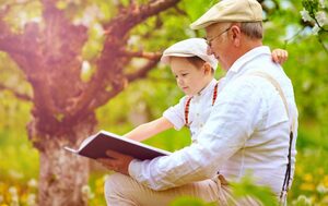 grandpa with hearing aids reads book to grandchild by a tree outdoors in elizabethtown