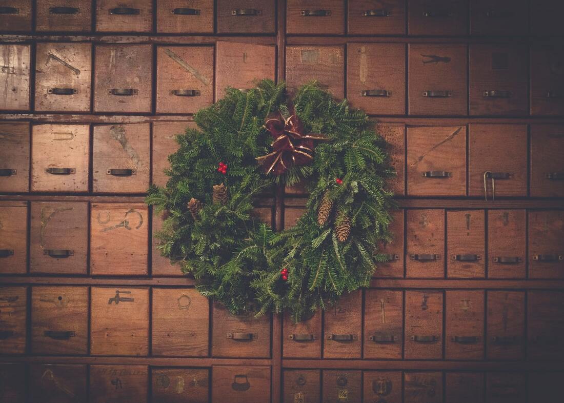 green_christmas_wreath_with_red_and_gold_bow_pinecones_red_berries_hanging_against_wall_of_wooden_drawerers_in_lancaster_pa