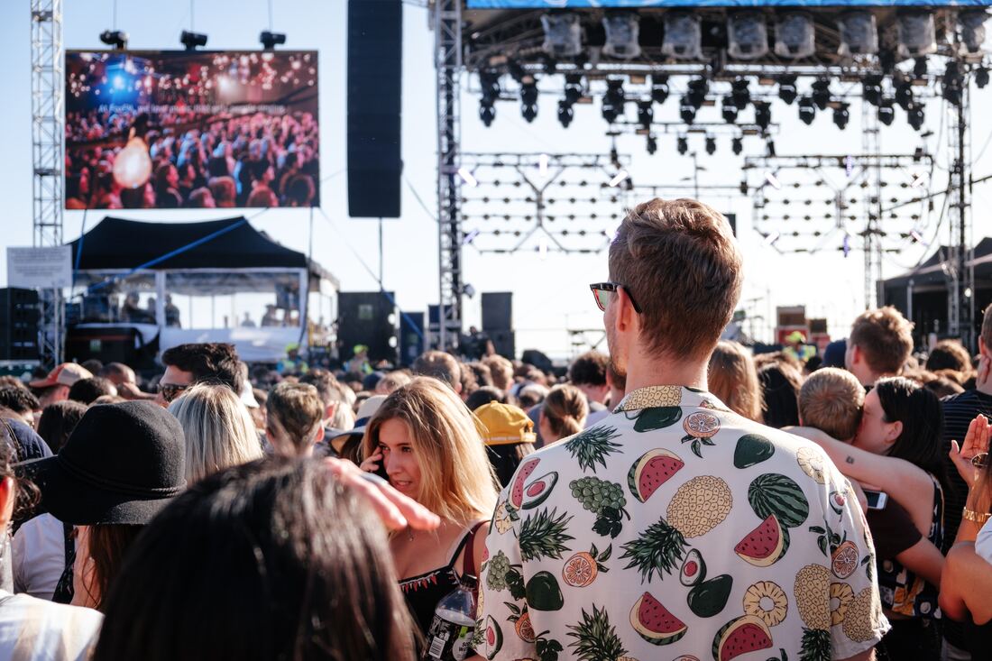 guy with tropical fruit shirt and earplugs stands far away from speakers at outdoor concert venue