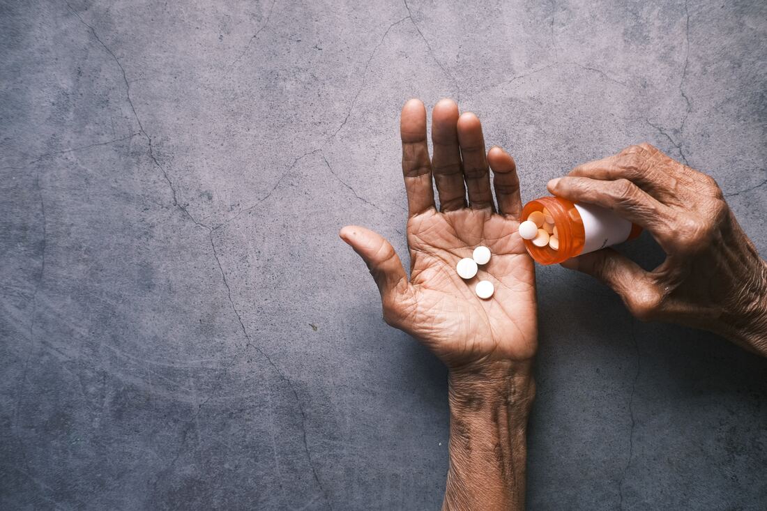 hand holds orange medication bottle and pours pills that cause hearing problems into other hand against fissured stone