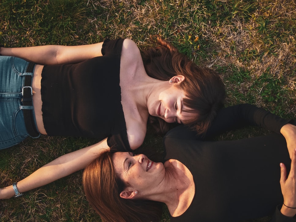 hard of hearing mother and daughter in black shirts lie in grass and face each other while smiling