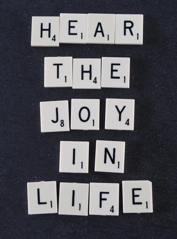 hear the joy in life spelled in scrabble pieces on top of black background