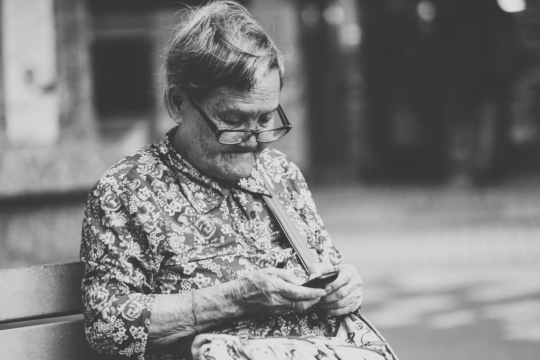 A woman with glasses sits on a bench using a hearing aid app on her smartphone.