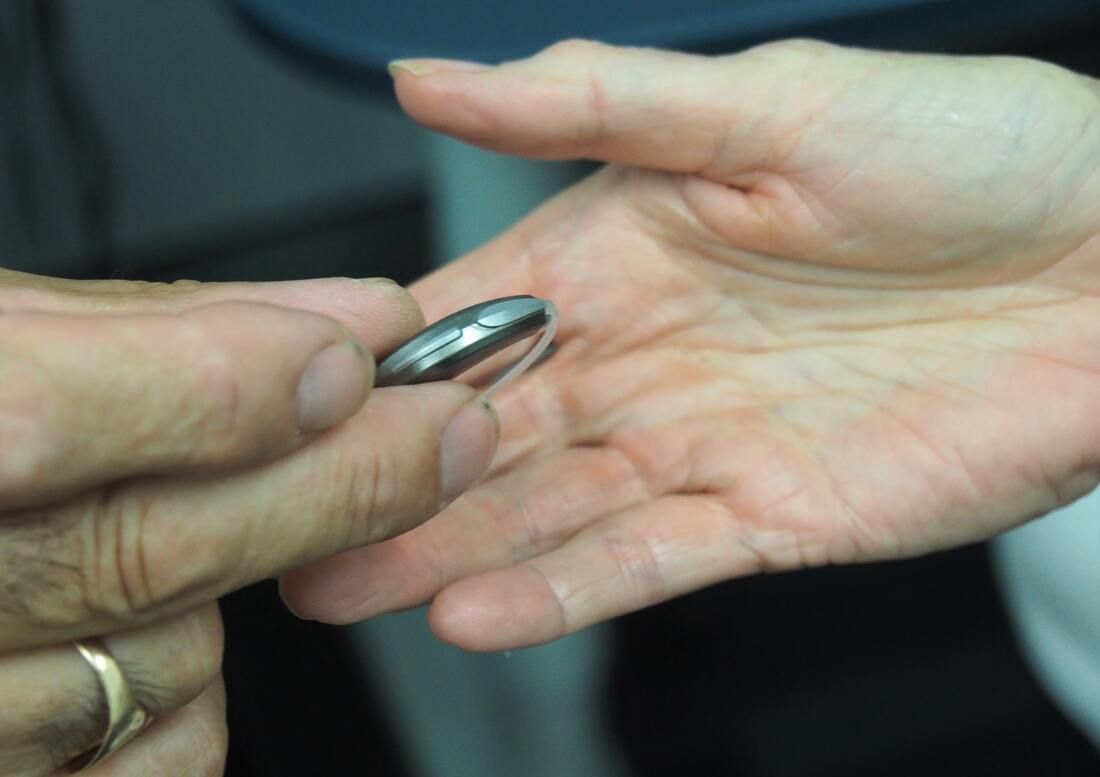 A man hands a used behind-the-ear hearing aid to a woman in a Lancaster hearing aid office.