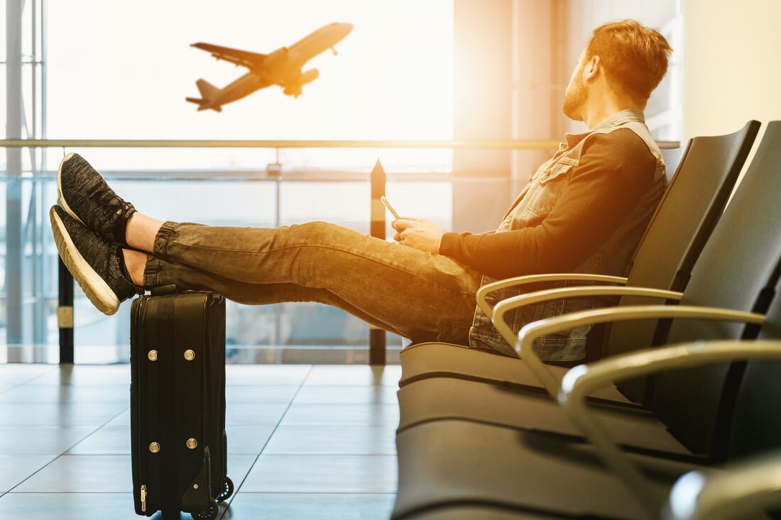 man sitting on gang chair with feet on luggage looking at airplane taking off