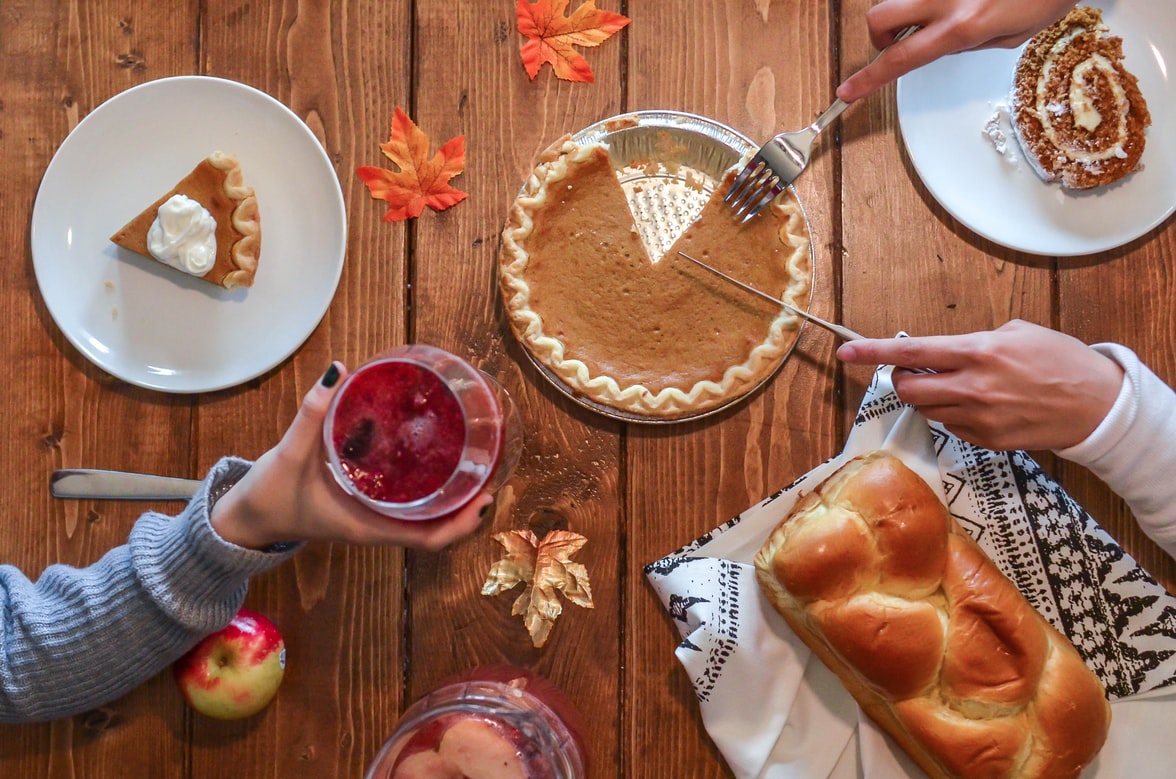 Thanksgiving_holiday_dessert_pumpkin_pie,_apple,_bread_hands_holding_utensils_and_a_glass_of_red_wine