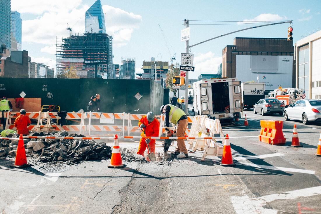 Construction workers fix a road in the city, while traffic halts on the side.