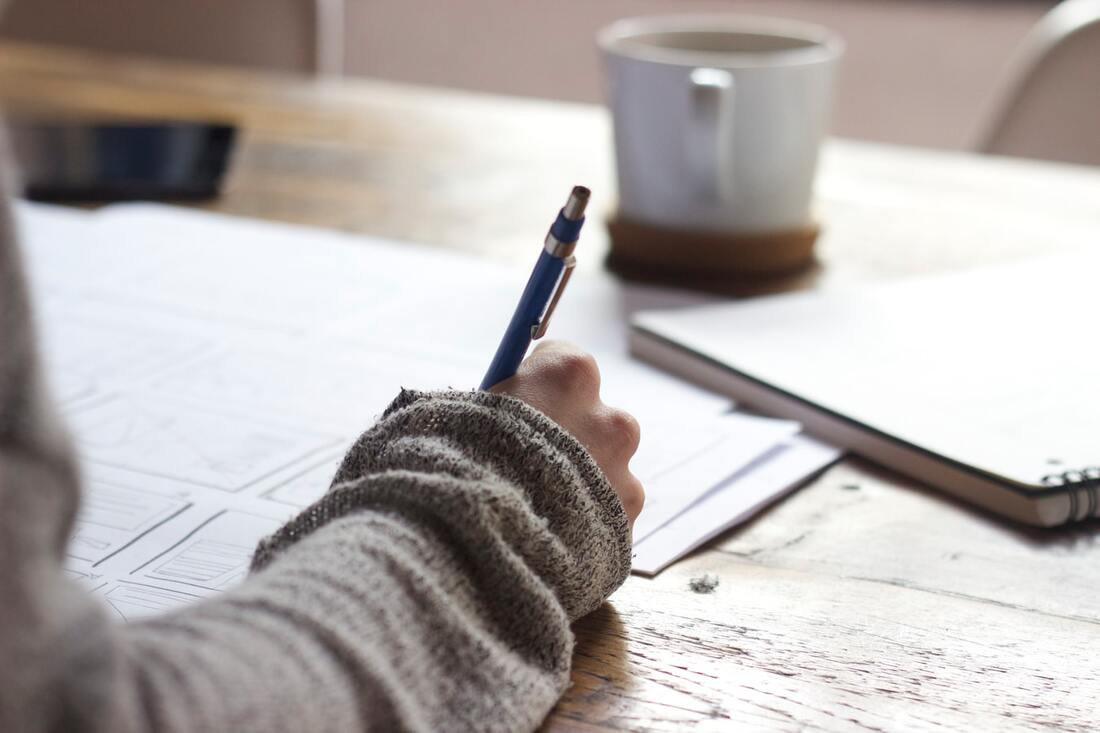 A person in a light grey sweater uses a writing utensil to write answers on a quiz.