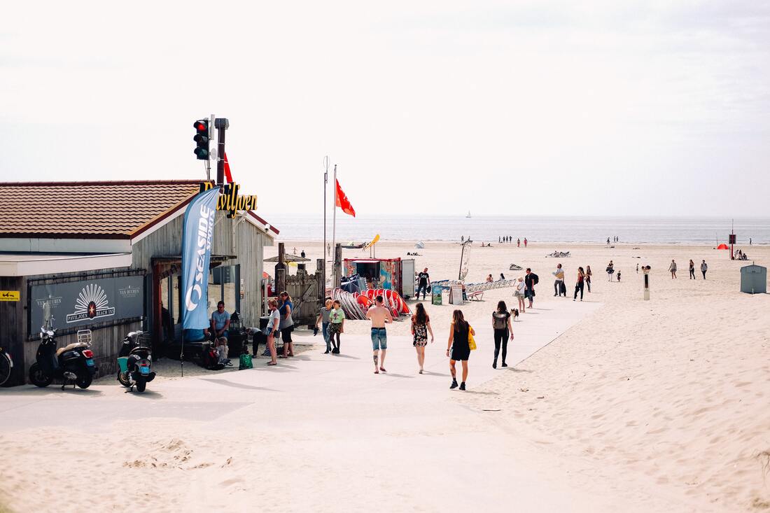 People walk through a beach equipment rental shop on the sand by the ocean.