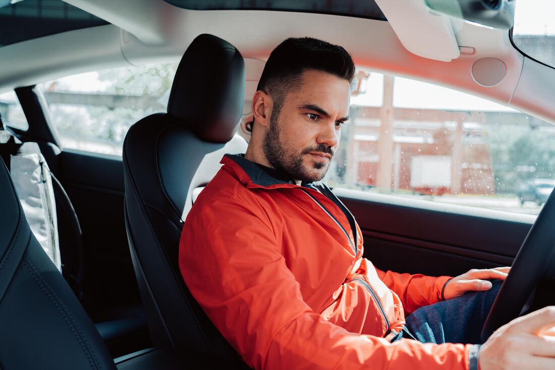 man in red jacket sitting on car's driver seat struggles to hear car engine