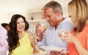 man drinking wine wears hearing aids at party with two women