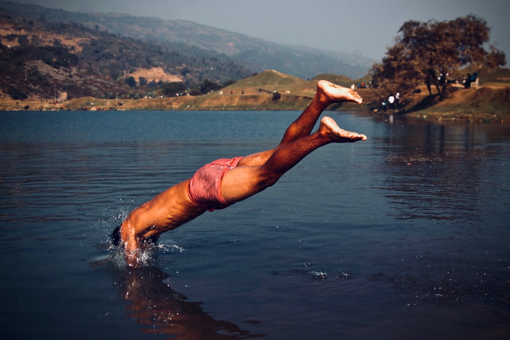 man in red swim trunks dives into water wearing custom earplugs