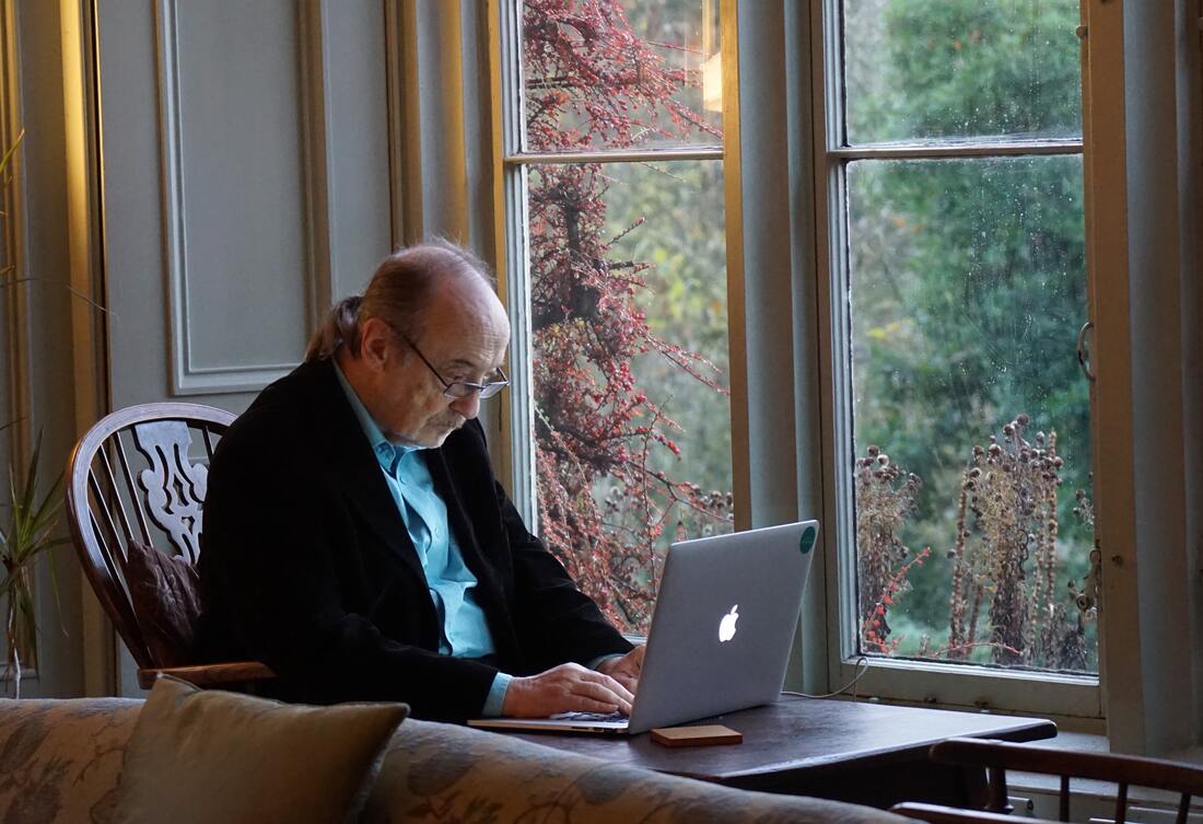 An elderly man with glasses uses a laptop to schedule a hearing test.