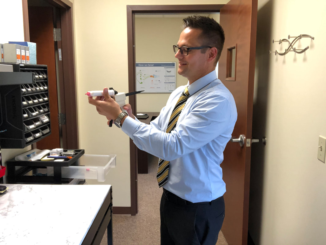 man uses impression gun to make customized hearing aid earmolds in strasburg hearing aid office