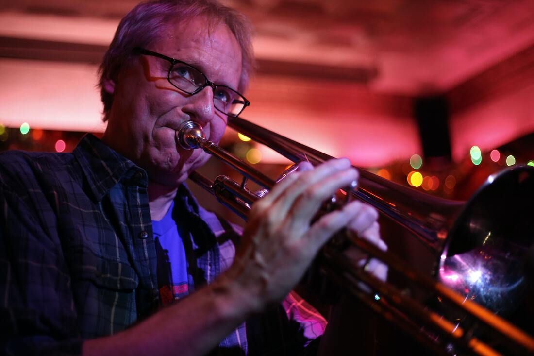 man with glasses and flannel shirt wears earplugs while playing trumpet