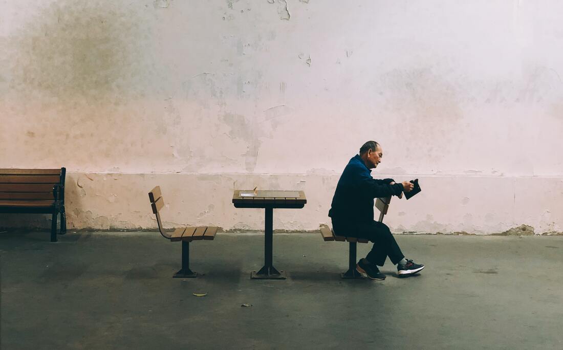 man with hearing aids sits backwards on bench seat by table and looks at a book
