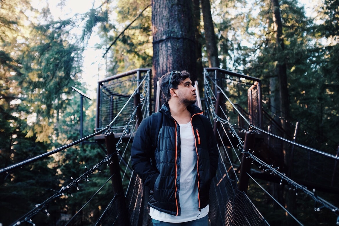 man with hearing loss stands on suspension bridge among trees in forest