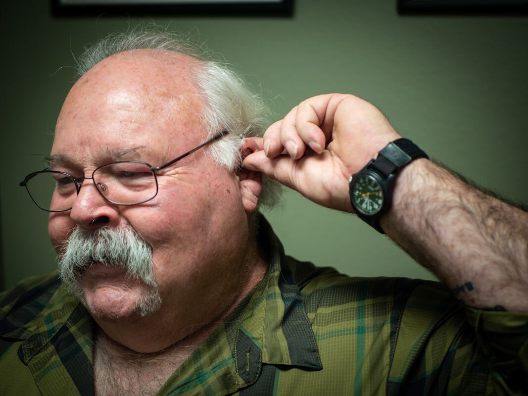 man with white mustache glasses and tinnitus adjusts hearing aid in ear