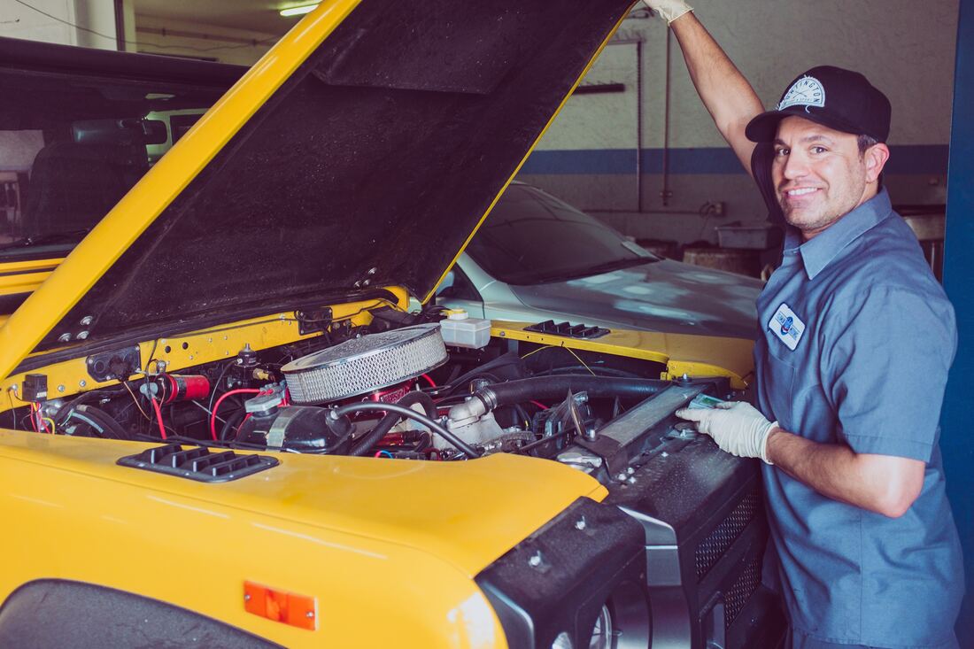 A mechanic smiles while pulling down the car hood on a yellow vehicle.