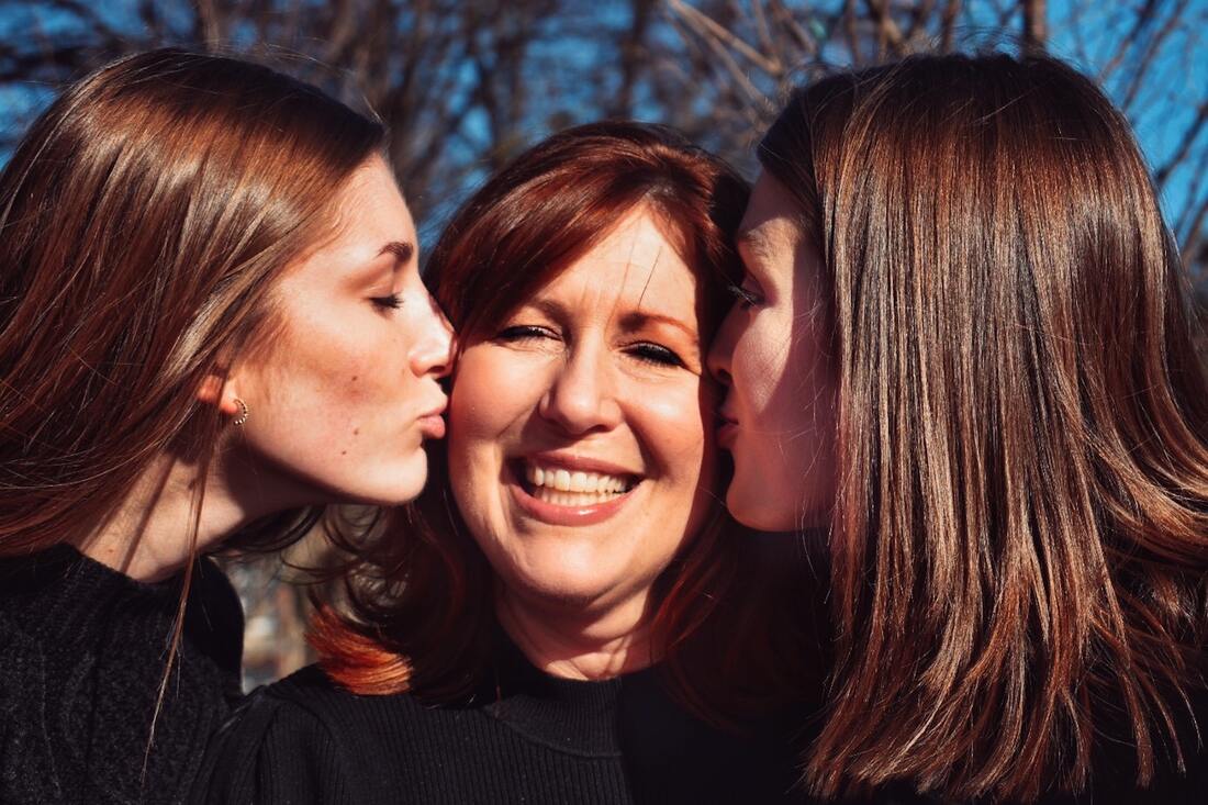 Two daughters kiss their mother, who has hearing loss.