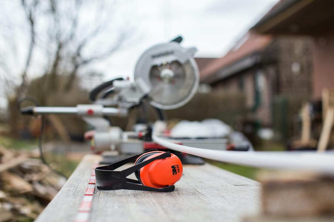 A pair of neon orange and black earmuffs rest by a table saw.
