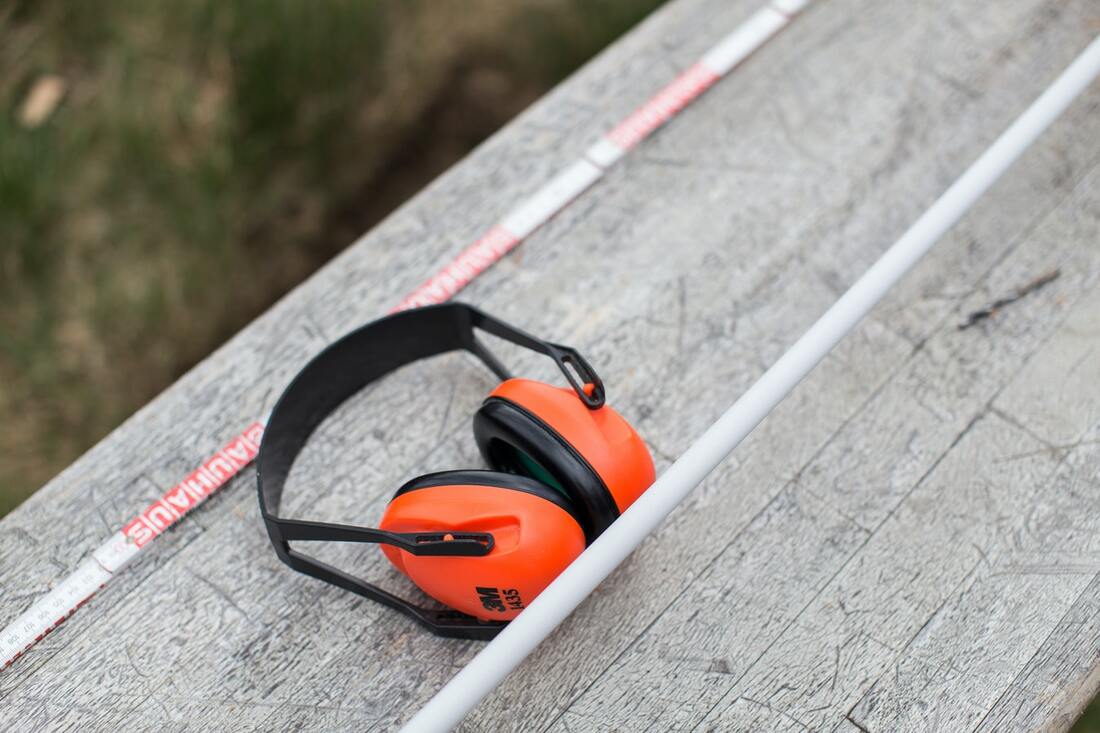 neon orange and black earmuffs on a wooden table outdoors used to protect hearing