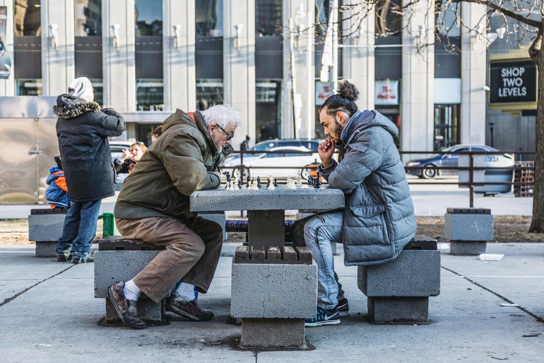old man with hearing aids plays chess with young man